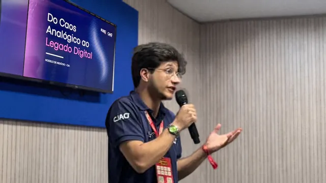 O presidente da CJA fala ao microfone diante do telão com o slide “Do Caos Analógico ao Legado Digital”, sobre o modelo de negócio da CJA.