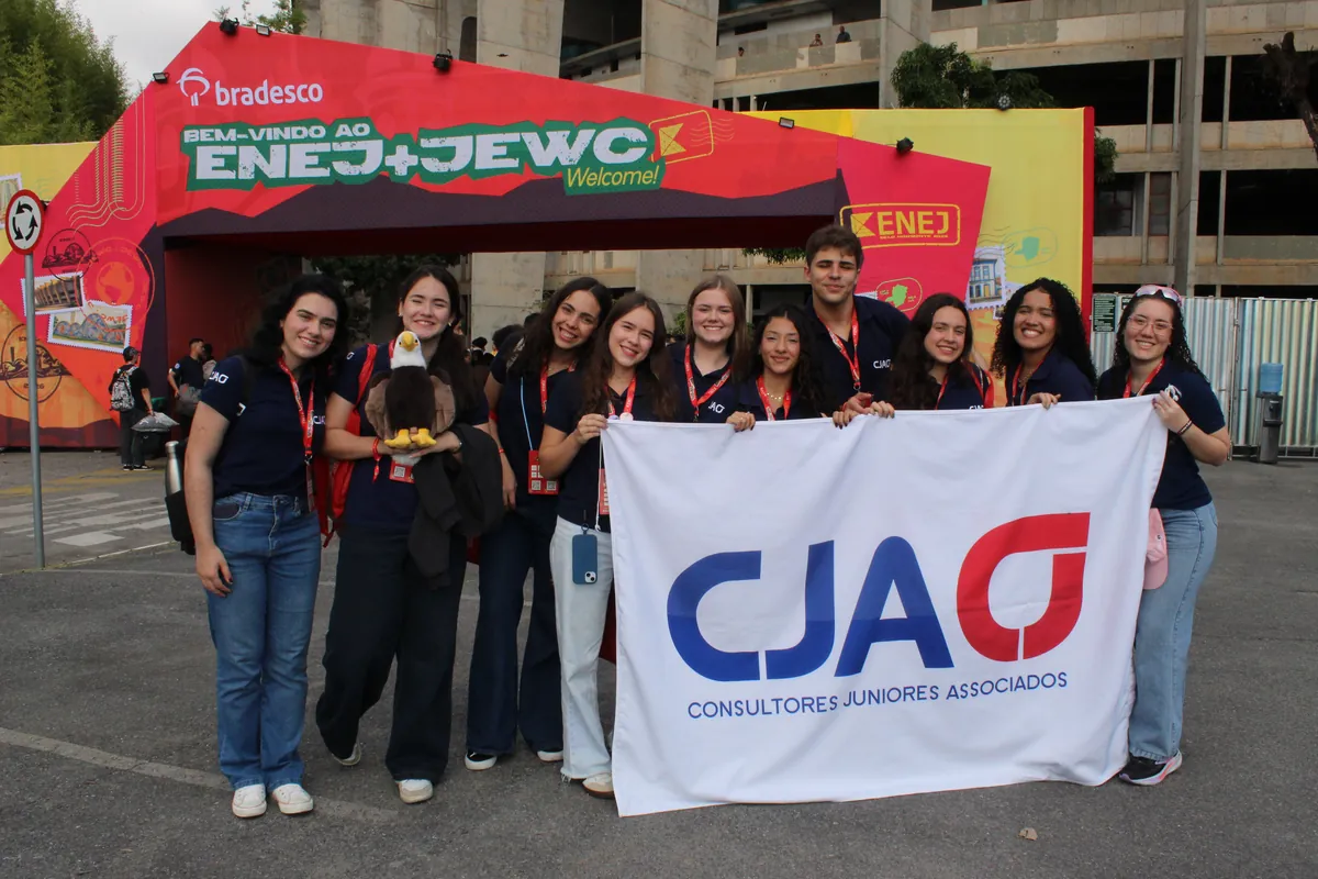 O time da CJA, de polo azul-marinho, com a bandeira da CJA na entrada do ENEJ 2026